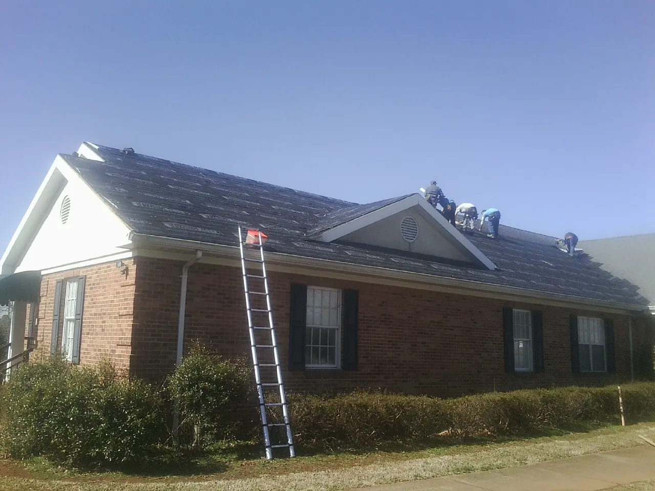 Crew tearing shingles off a brick ranch roof with a ladder set — Emergency Roof Repair work by our crew in Southbridge