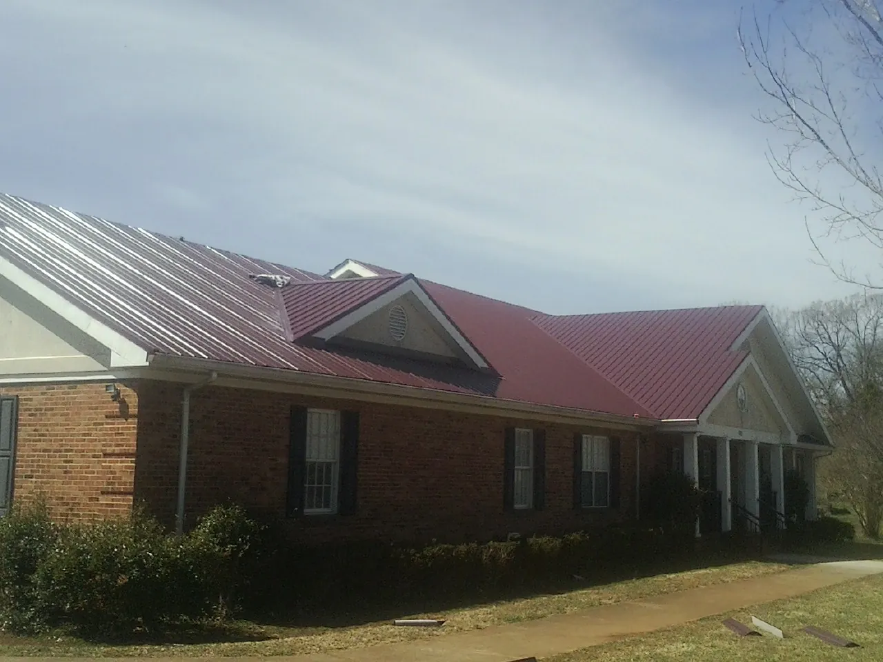 Red metal roof with gabled entries on a long brick building, from a Hail Damage Roof Repair job in Southbridge