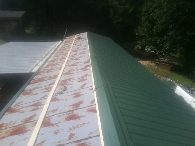 Old rusted panels beside newly installed green metal roofing — Wind Damage Roof Repair by Roofing Brothers in Southbridge