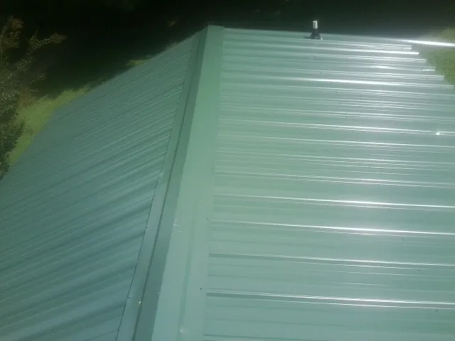 New green metal panels meeting at the ridge of a roof — Flat Roof Repair work by our crew in Southbridge