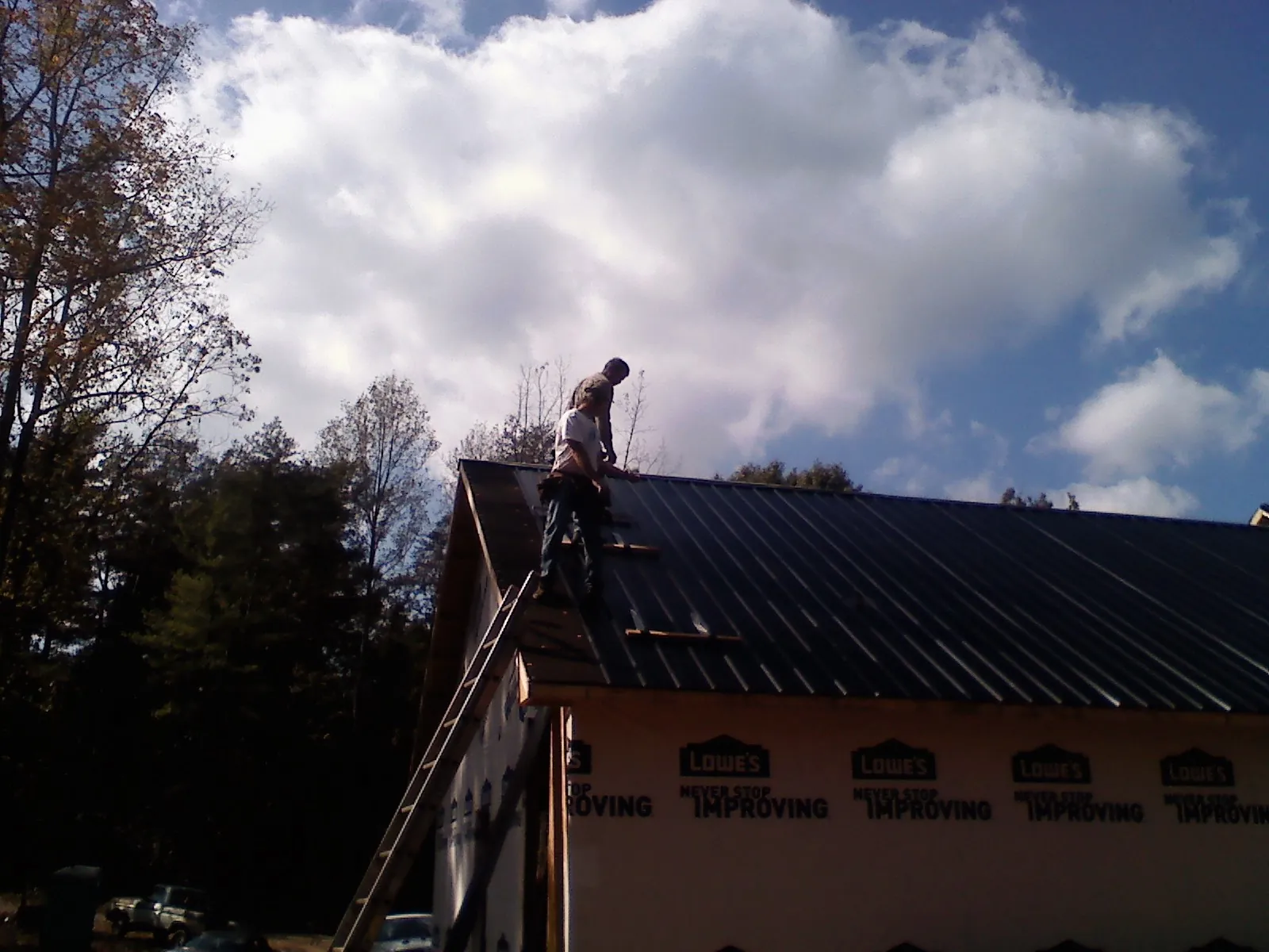 Roofer fastening dark metal panels high against a cloudy sky, from a Roof Inspection job in Southbridge
