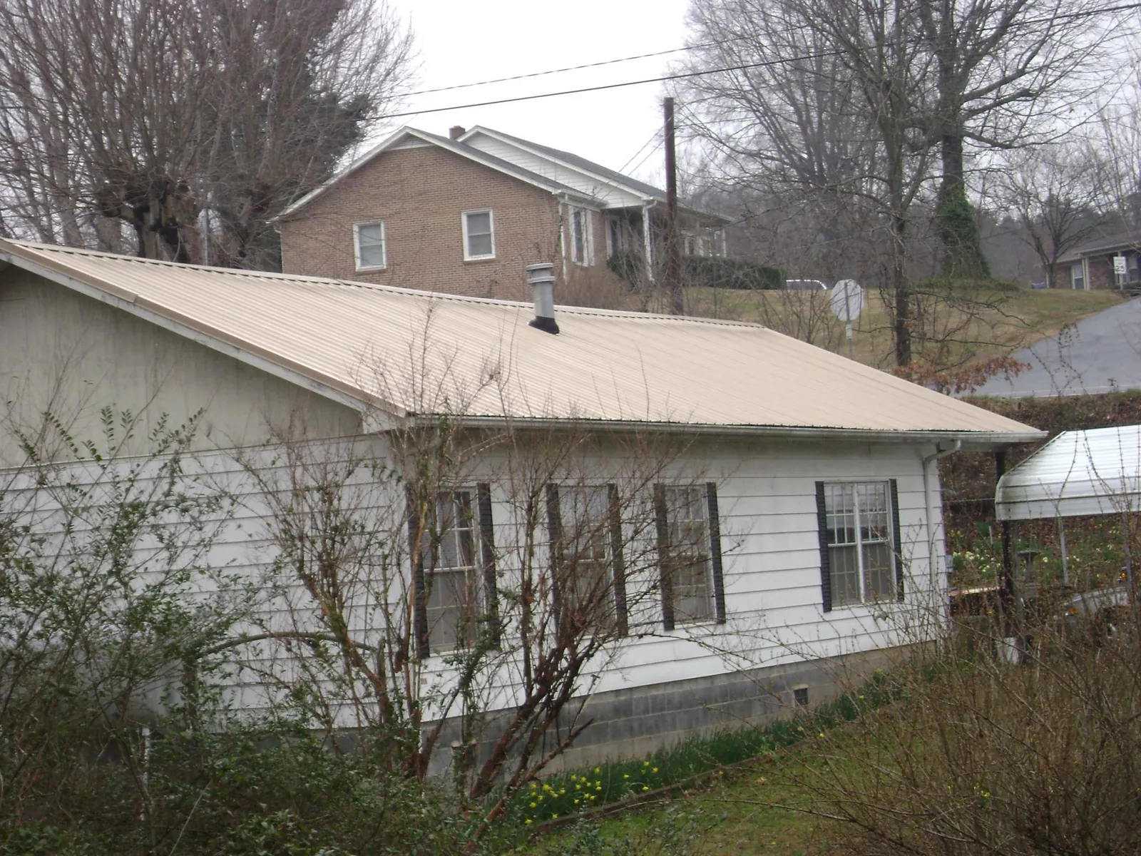 Tan metal roof on a white sided house set into a hillside — Commercial Roofing by Roofing Brothers in Southbridge
