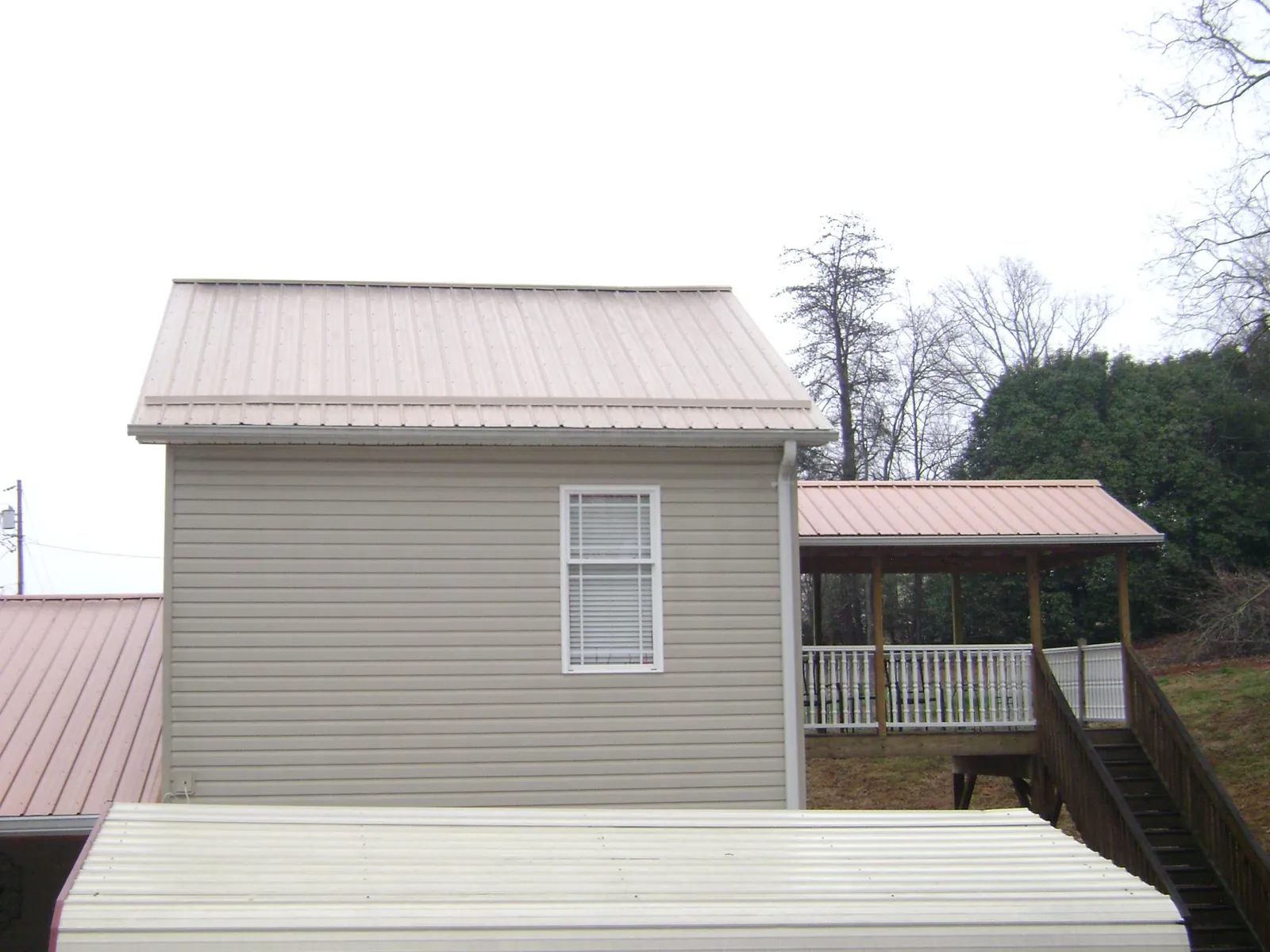 Tan metal roofs on a two story addition and attached porch, from a Roof Replacement job in Southbridge