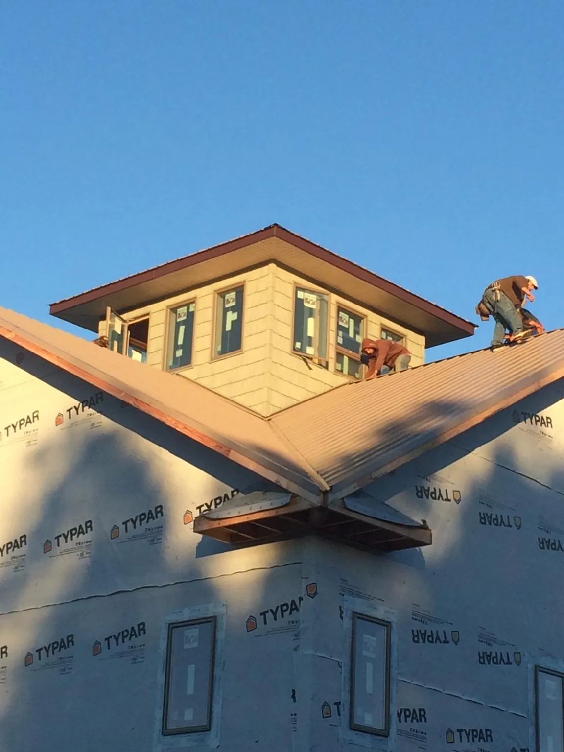 Roofers working around a rooftop cupola on a new metal roof at sunset — Roof Waterproofing in Southbridge by Roofing Brothers